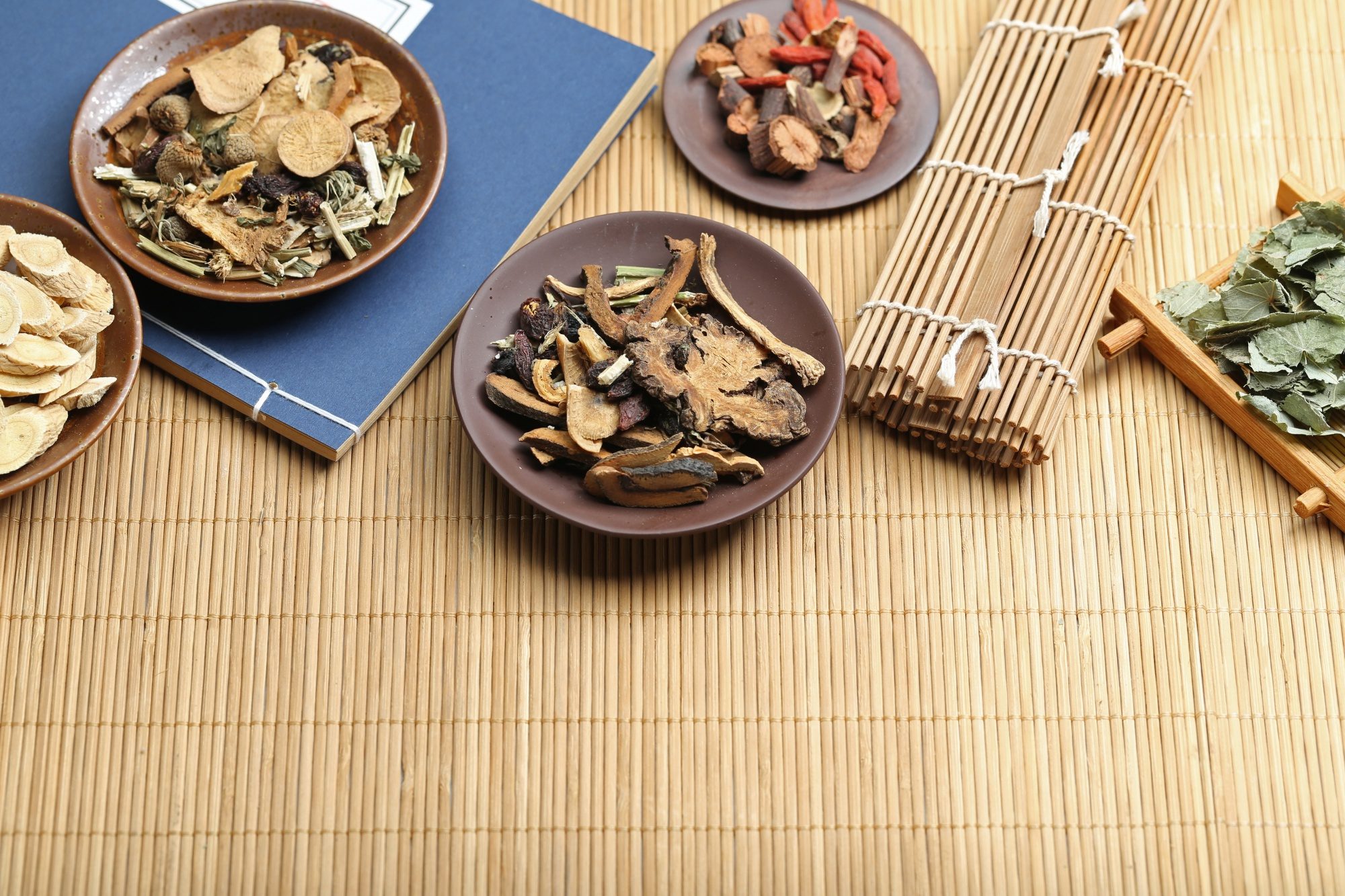 A flat lay of traditional Chinese medicine herbs on wooden plates with bamboo mat background, symbolizing holistic healing and acupuncture marketing themes.
