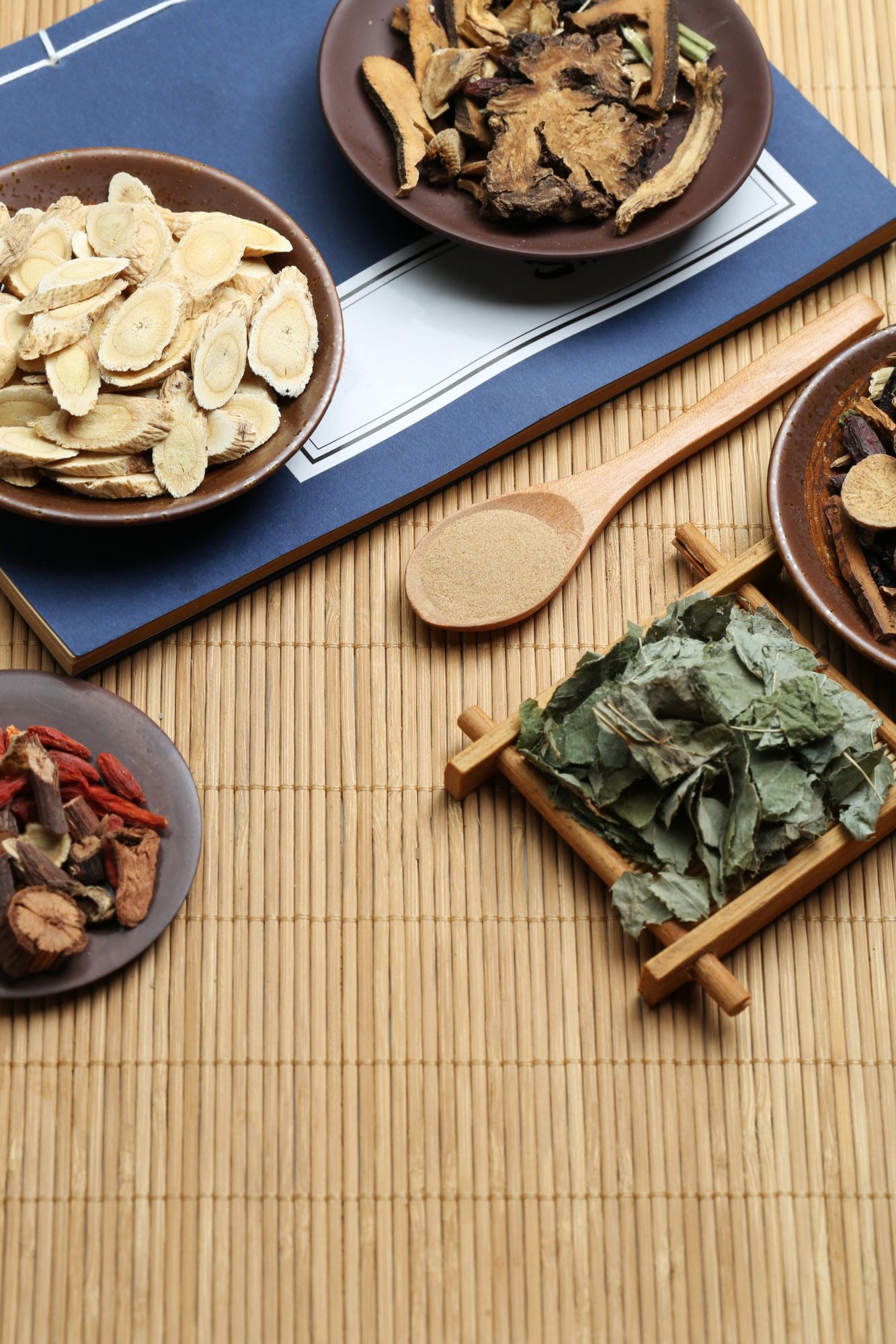 Traditional Chinese medicine herbs displayed on bamboo mat with wooden spoon, representing natural healing and wellness.